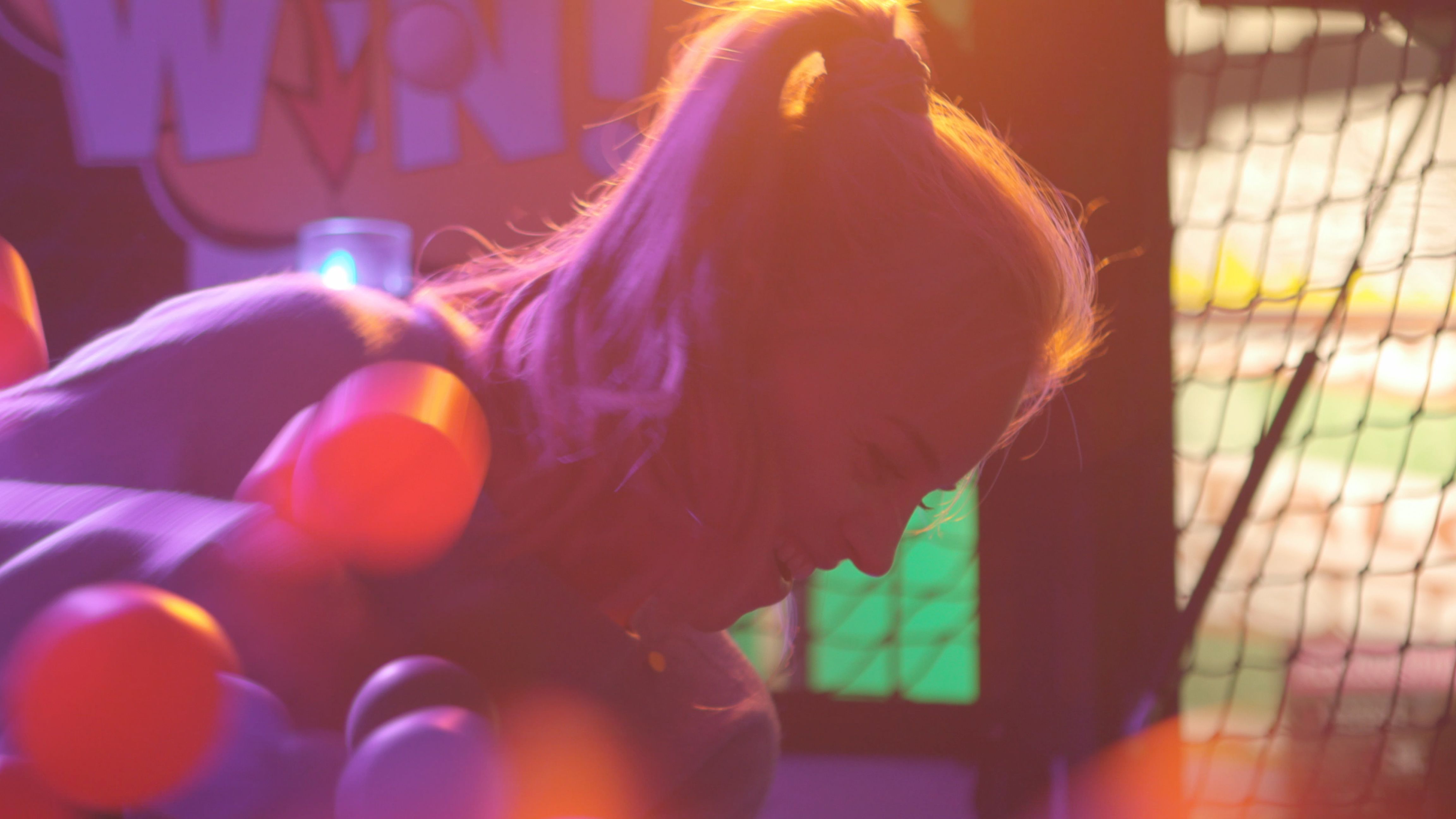 A woman leans into a ball pit lit in pink and orange during Showkees