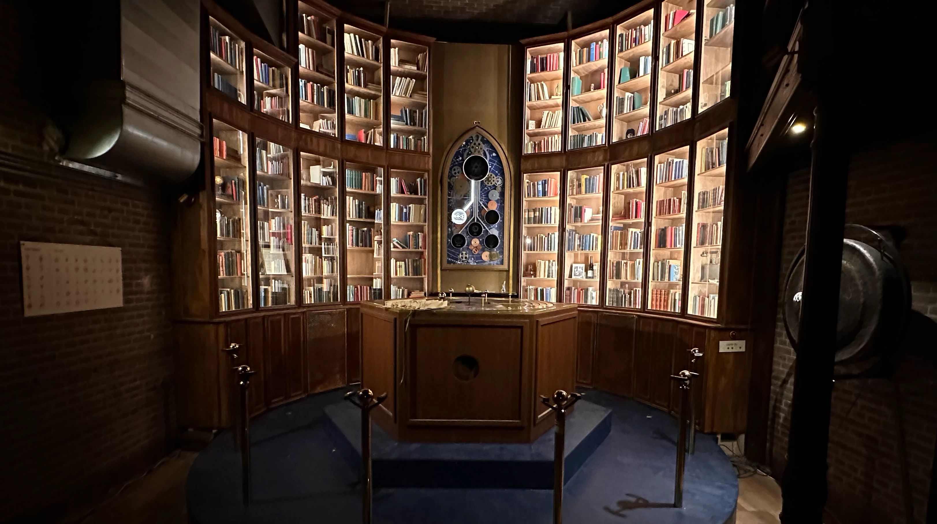 A round library room with tall bookcases, a stained-glass window and a wooden altar in the middle