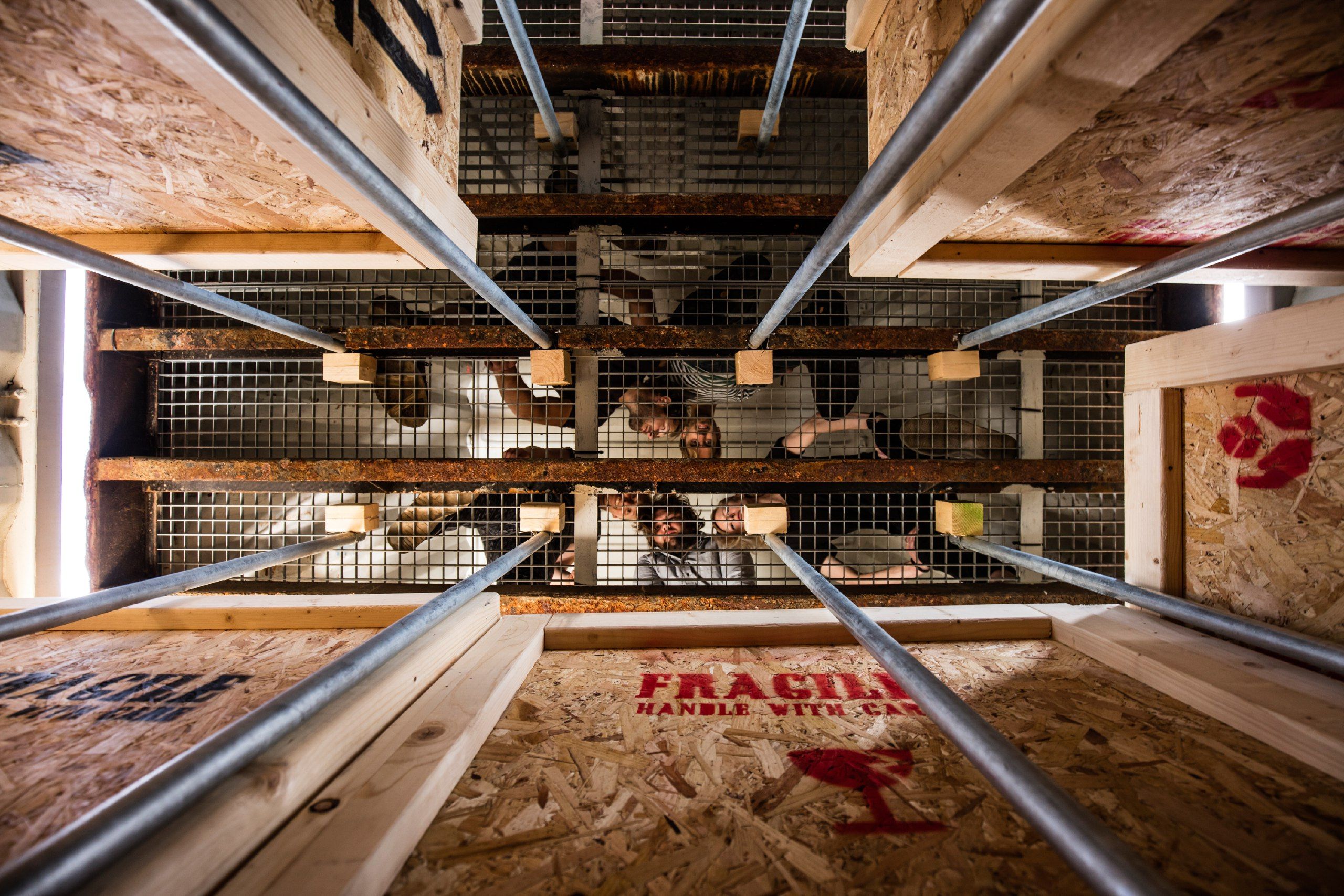 Players seen from below through a metal grid inside a wooden shipping crate marked fragile